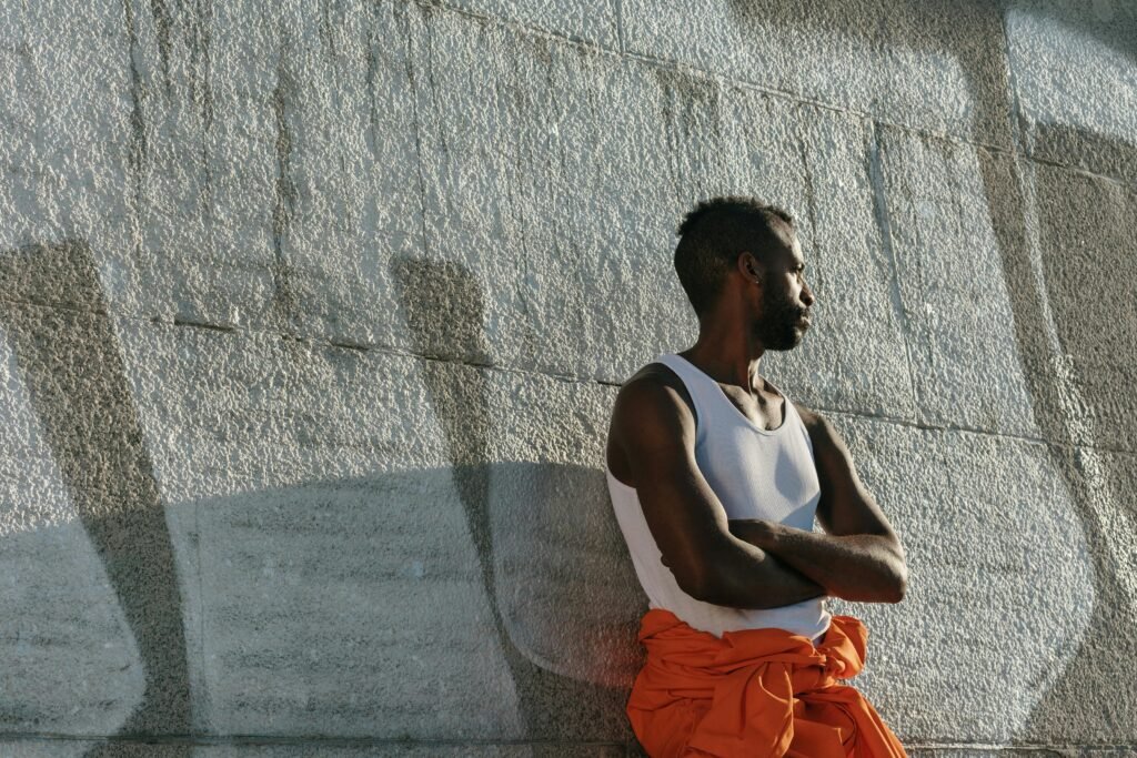 Stylish man in urban setting leaning against a graffiti-covered wall, arms crossed, gazing away.